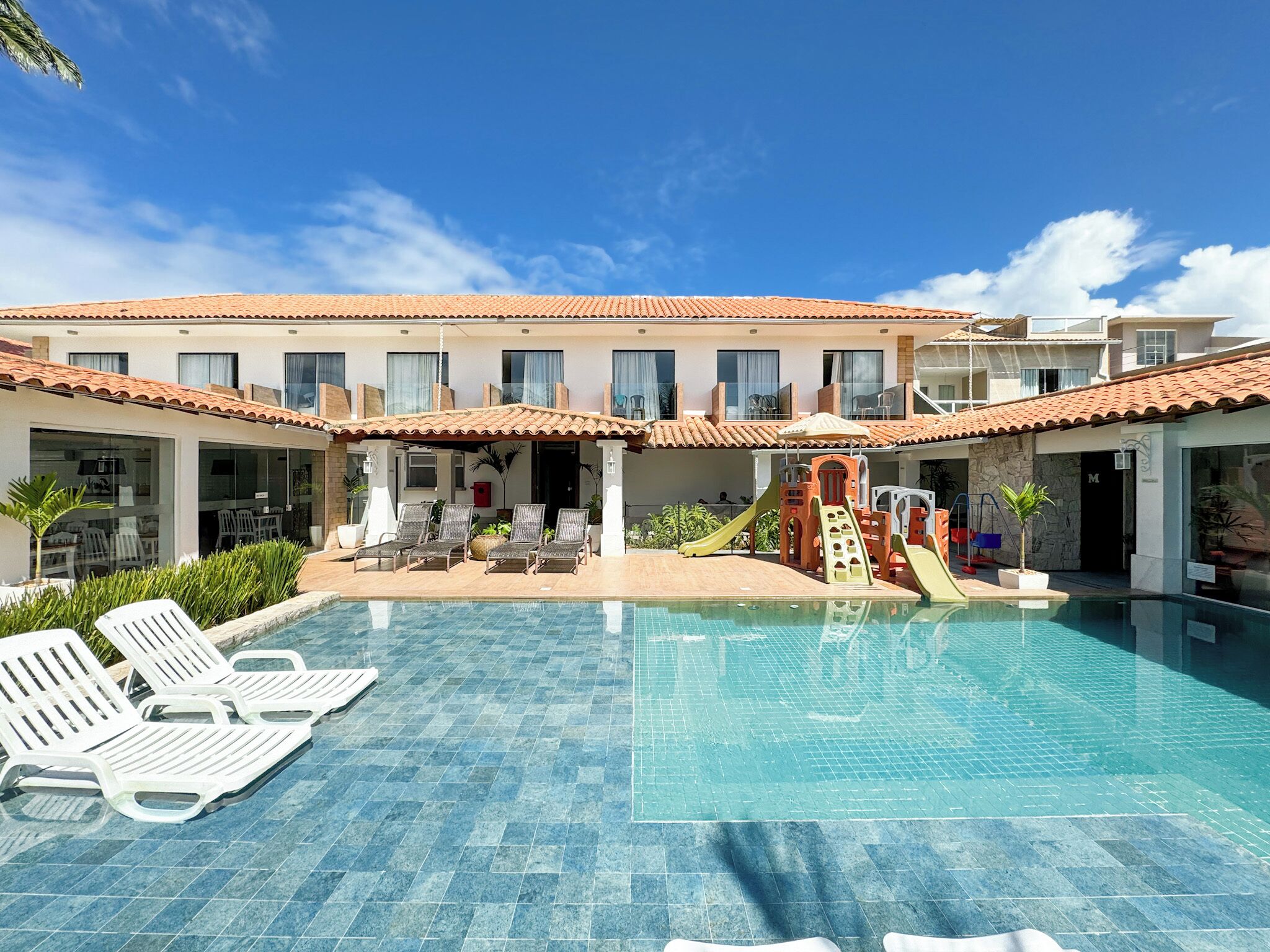 A hotel with a swimming pool, lounge chairs, and a children's play area.