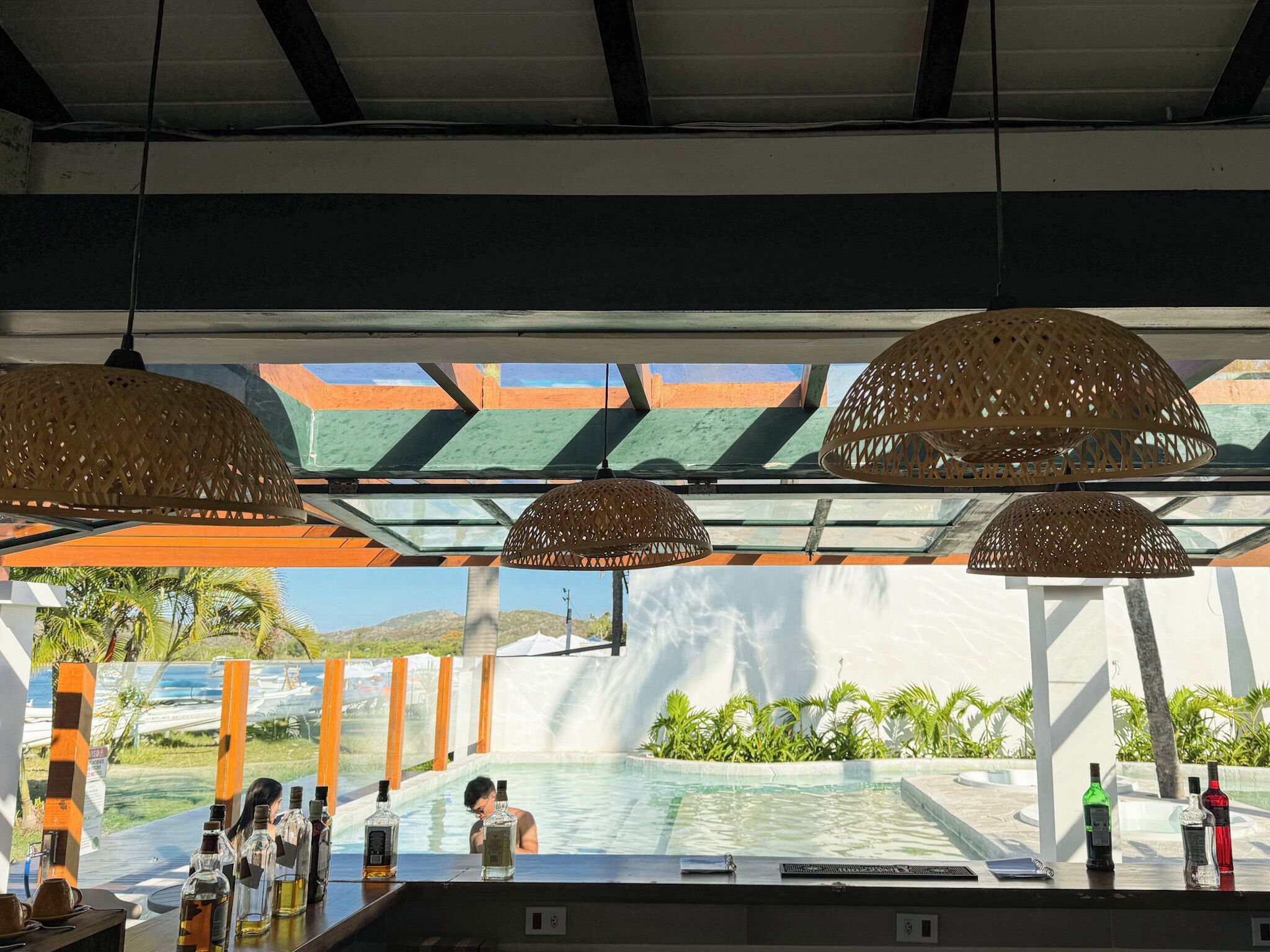 A poolside bar with bottles of alcohol, a person in the water, and a view of a waterfall.