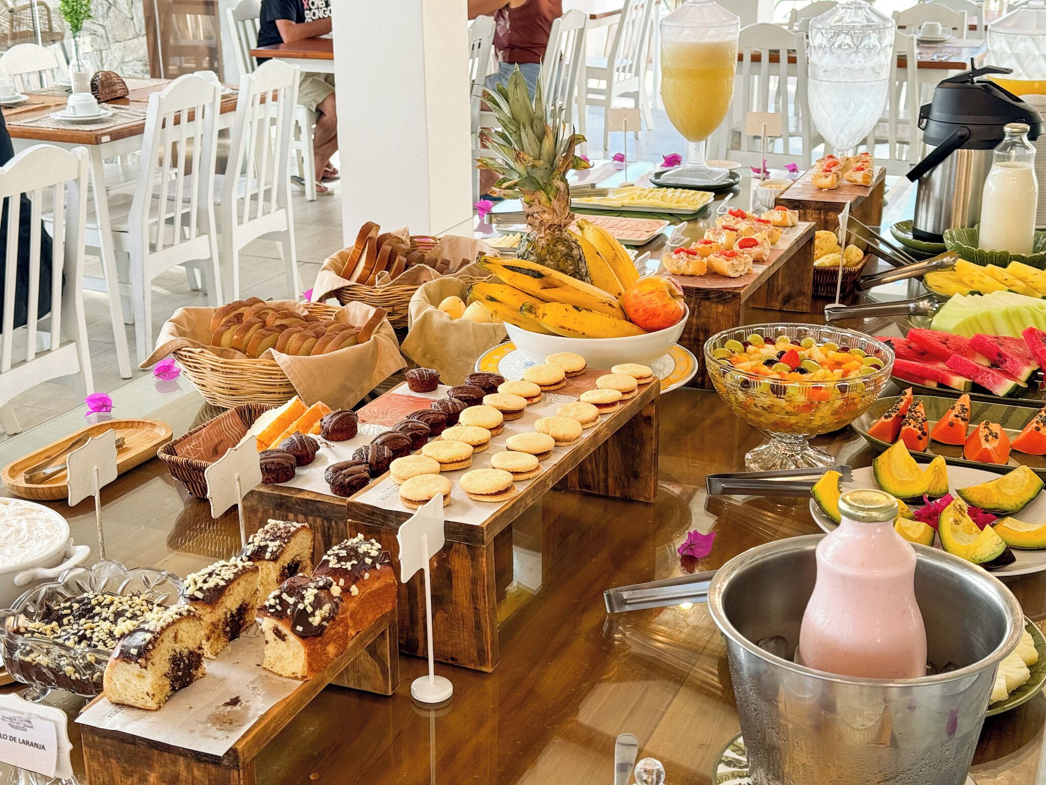 A buffet with various food items including bread, pastries, fruits, and a beverage dispenser.