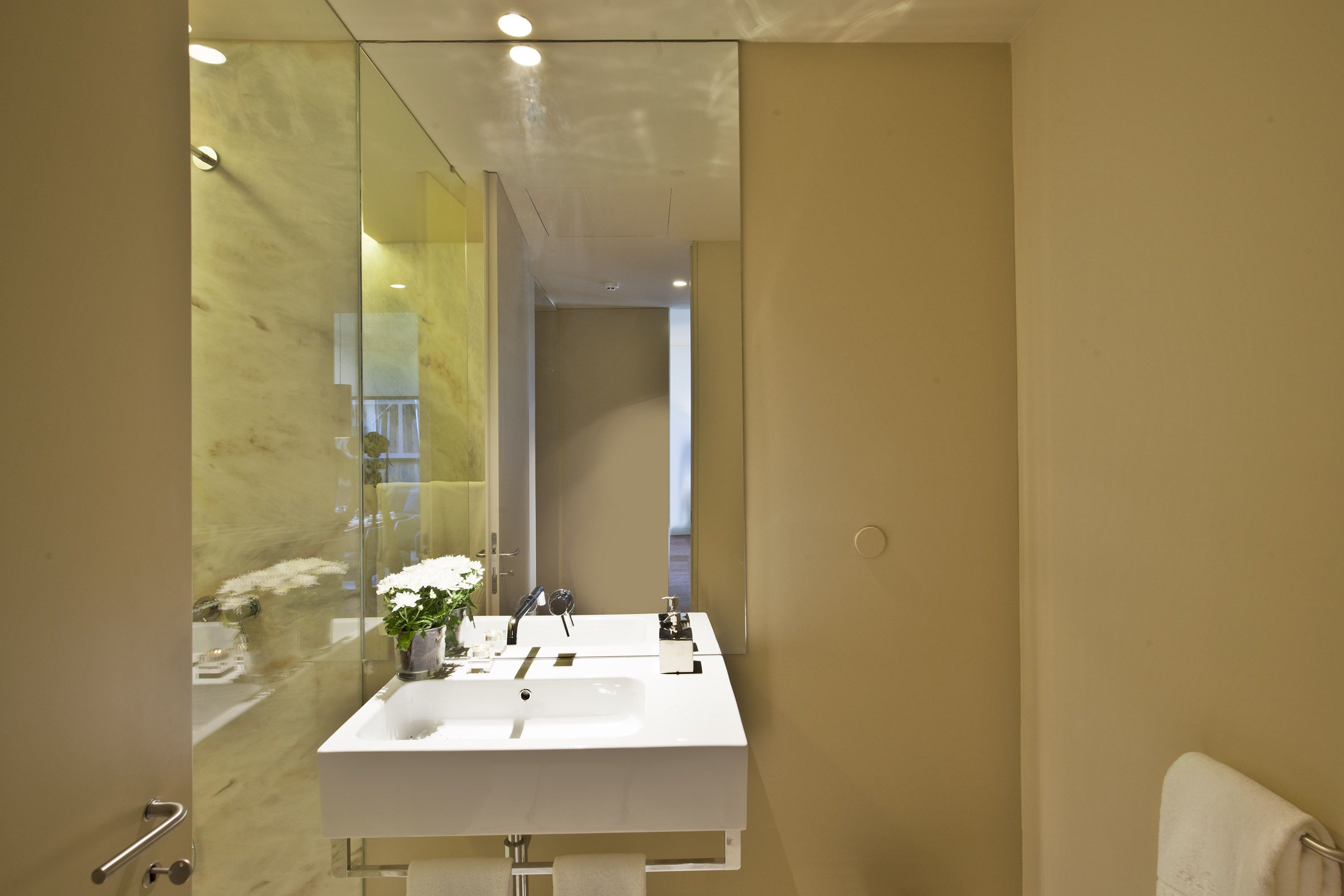 A modern bathroom with a large mirror, a white sink, and a towel rack.