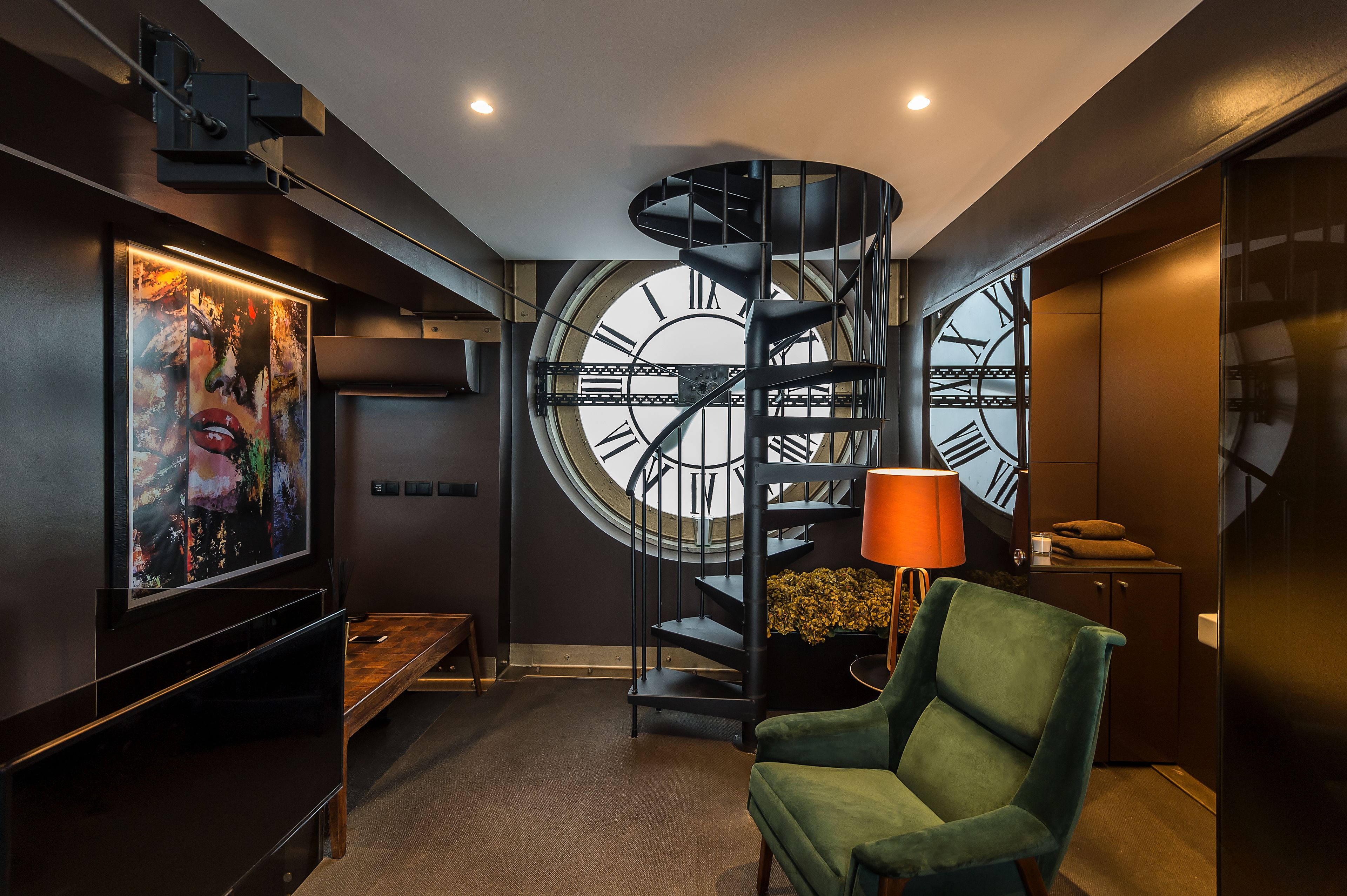 A modern interior with a spiral staircase, a large clock, and a green armchair.