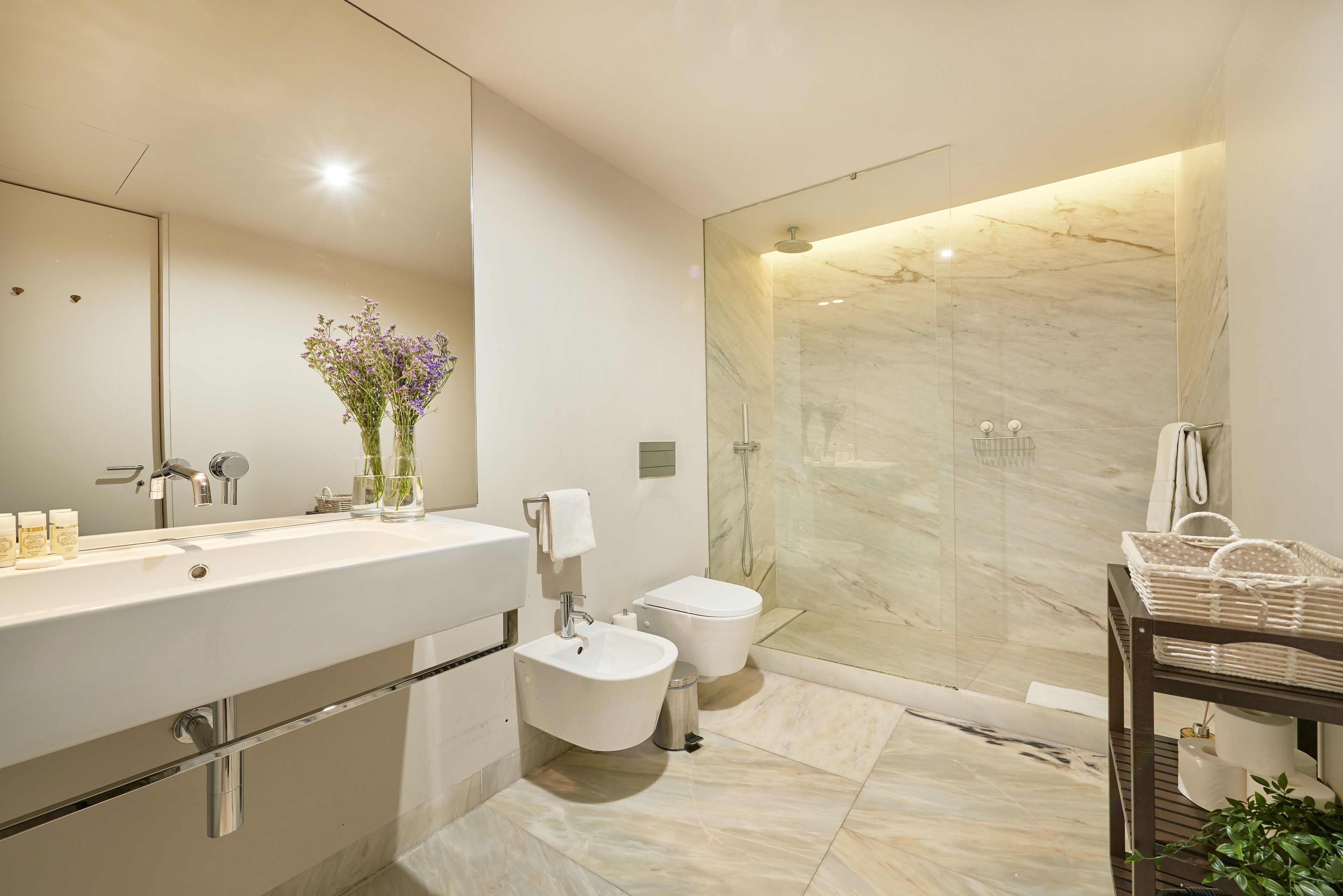 A modern bathroom with a large sink, a bidet, a toilet, and a glass-enclosed shower area.