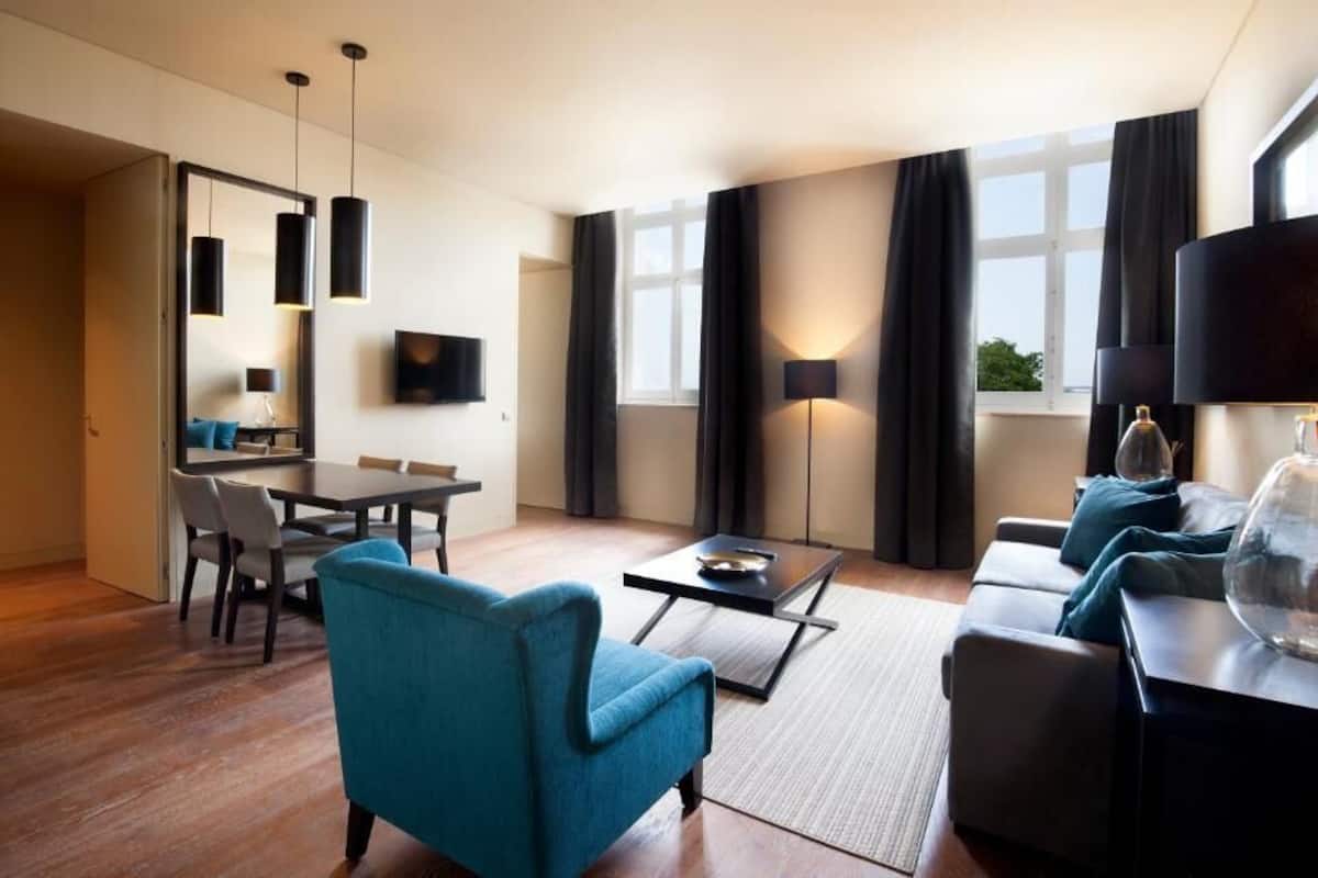 A modern living room with a sofa, armchair, dining table, and TV.