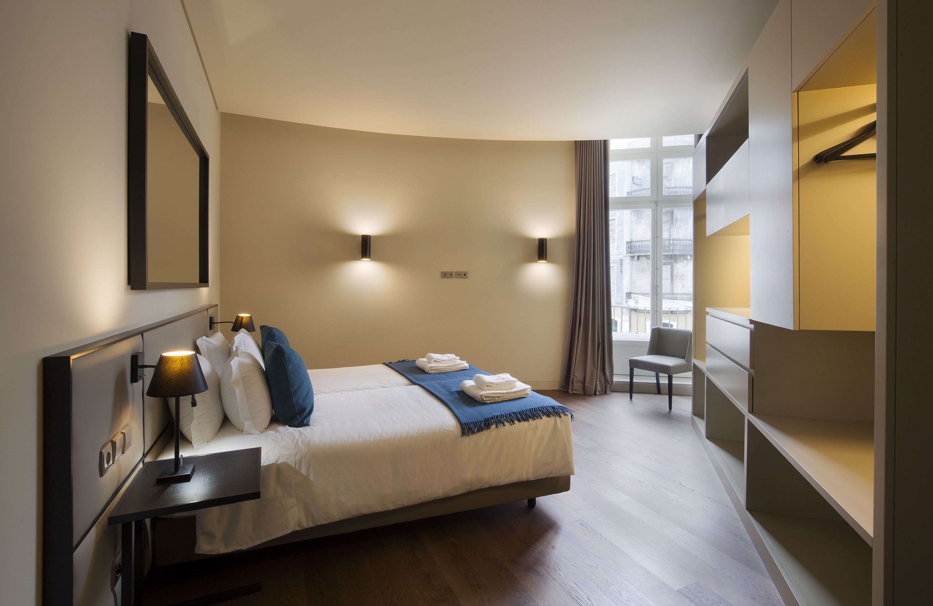 Una habitación de hotel moderna con cama, mesita de noche, lámpara y una silla.