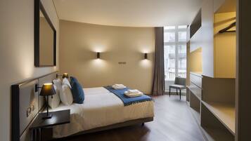 Une chambre d’hôtel moderne équipée d’un lit, d’une table de chevet, d’une lampe et d’une chaise.