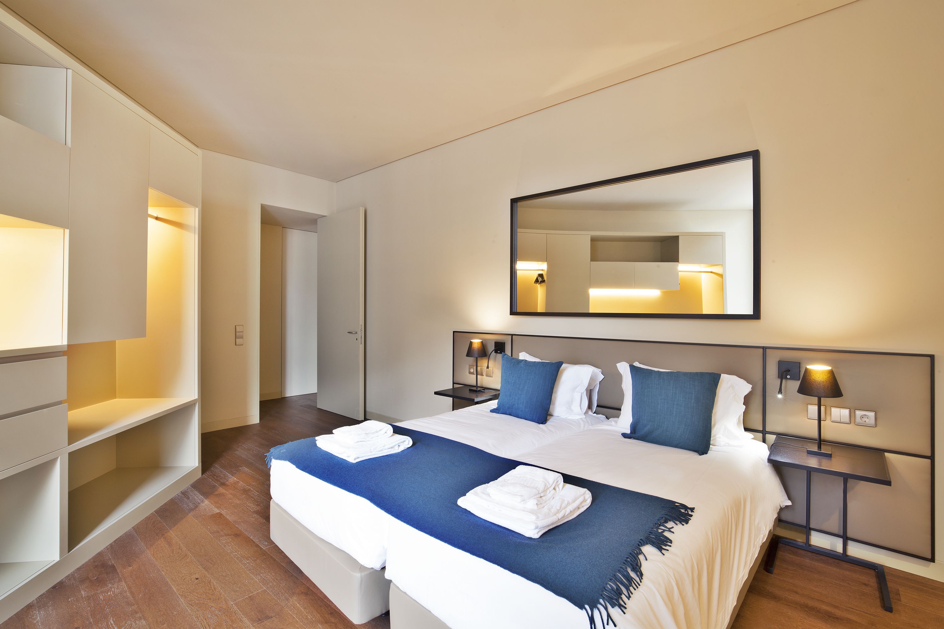 A hotel room with a large bed, two bedside tables with lamps, a wardrobe, and a mirror on the wall.