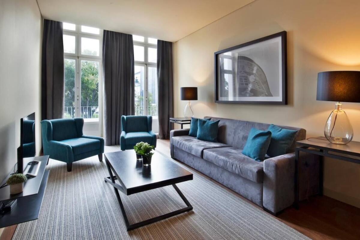 A modern living room with a grey sofa, two teal armchairs, a coffee table, a TV, and a framed picture on the wall.