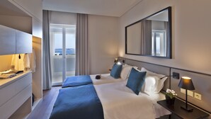 Een hotelkamer met een bed, een bureau, een spiegel en uitzicht op zee.