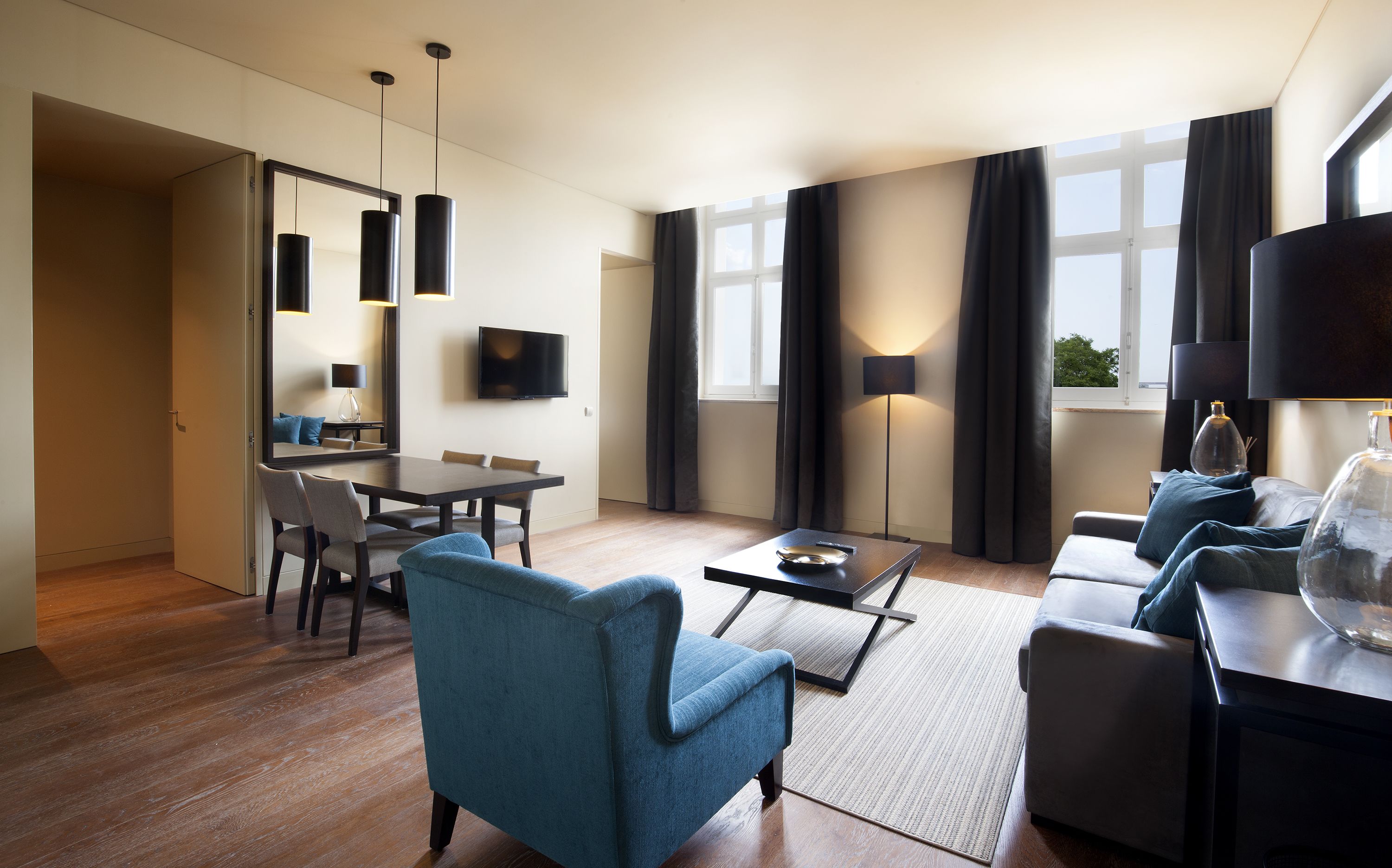 A modern living room with a dining area, a flat-screen TV, and a large window with curtains.