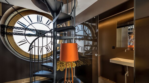 Een modern interieur met een grote wandklok, een spiltrap en een badkamer met wastafel en spiegel.