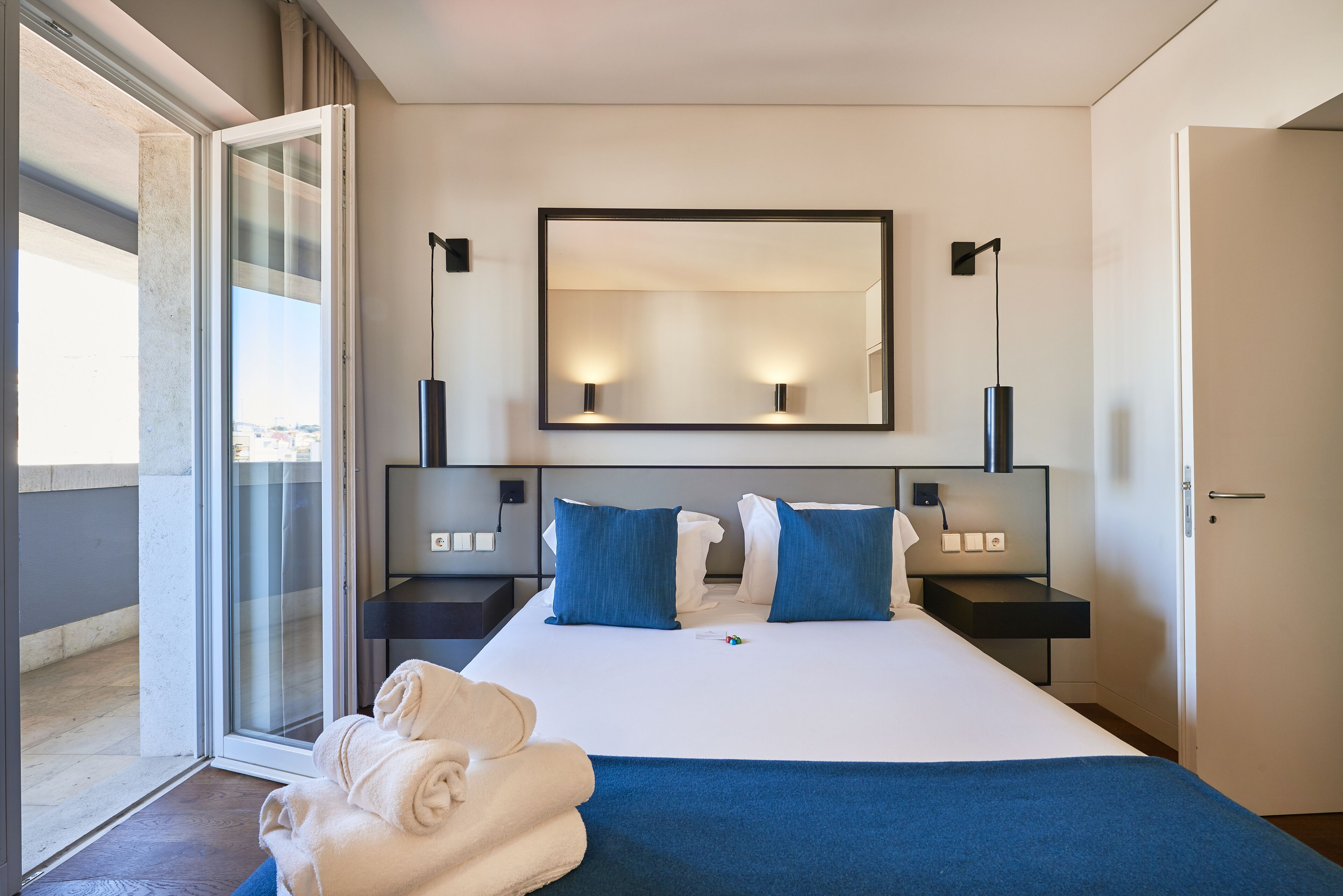 Ein modernes Hotelzimmer mit einem großen Bett, einer Glastür, die auf einen Balkon führt, und einem großen Spiegel über dem Bett.