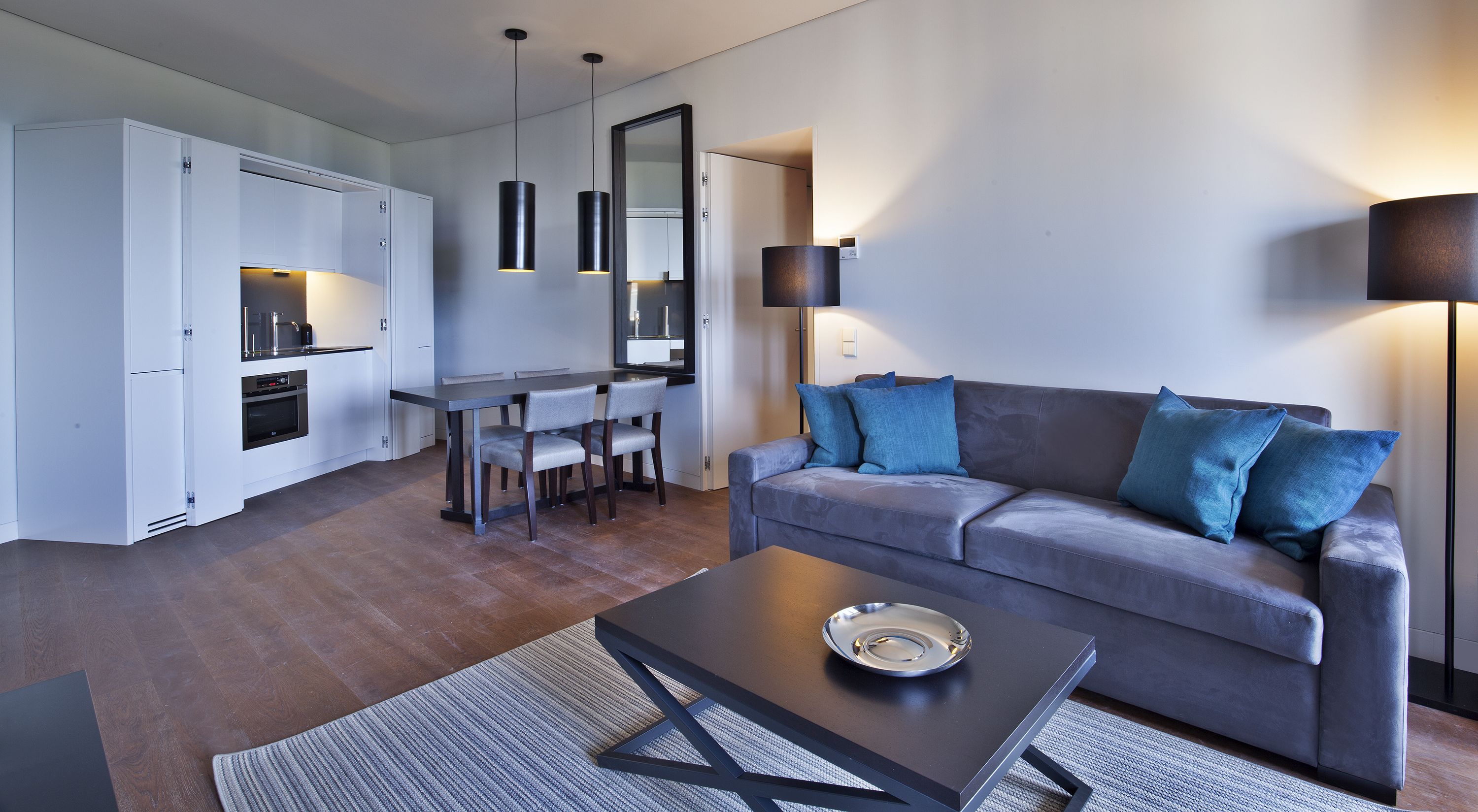 A modern living room with a grey sofa, blue cushions, a coffee table, and a dining area with a table and chairs.