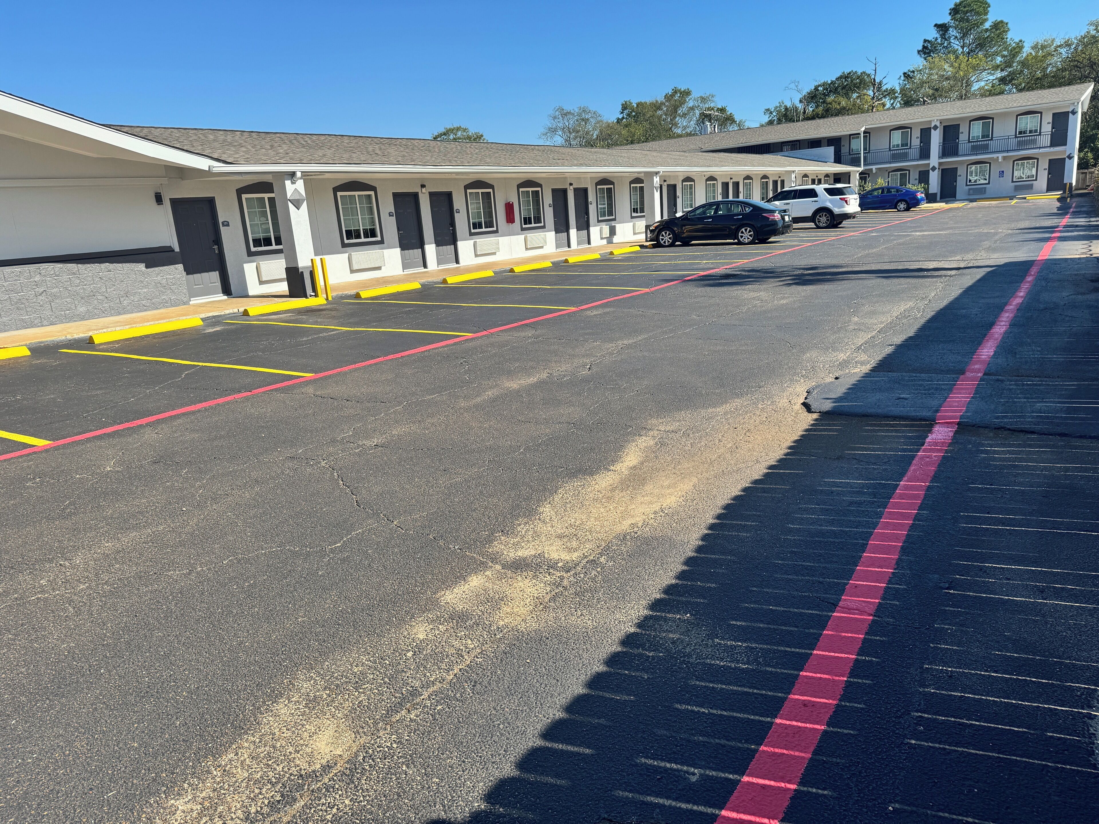 Un parking avec des places délimitées et un bâtiment doté de nombreuses portes et fenêtres.