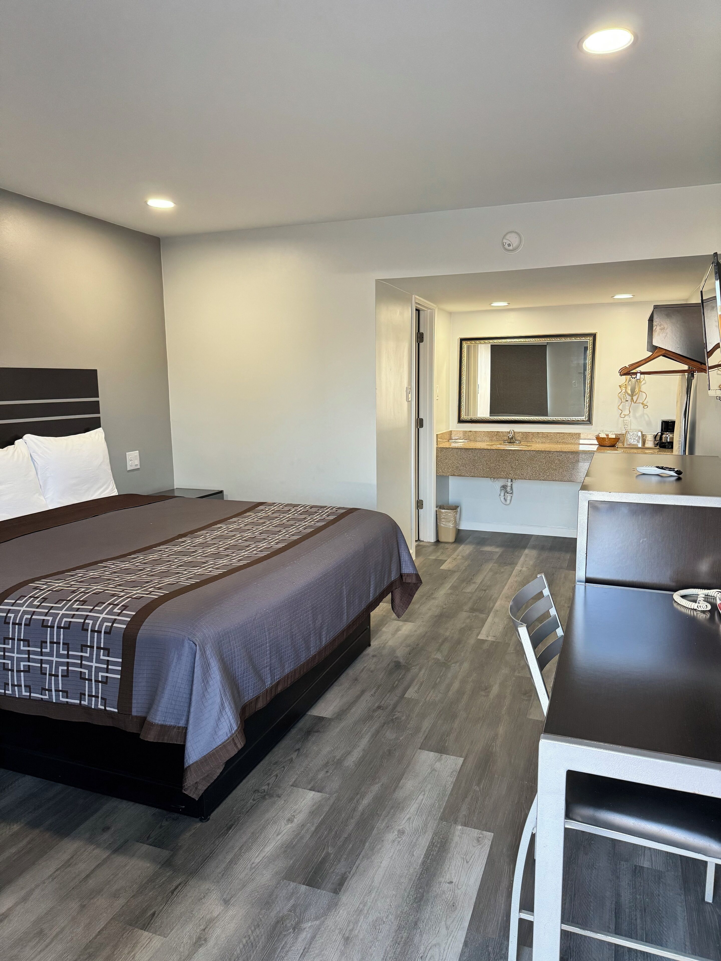A hotel room with a bed, a desk, a chair, a dresser, a mirror, and a bathroom visible through an open door.