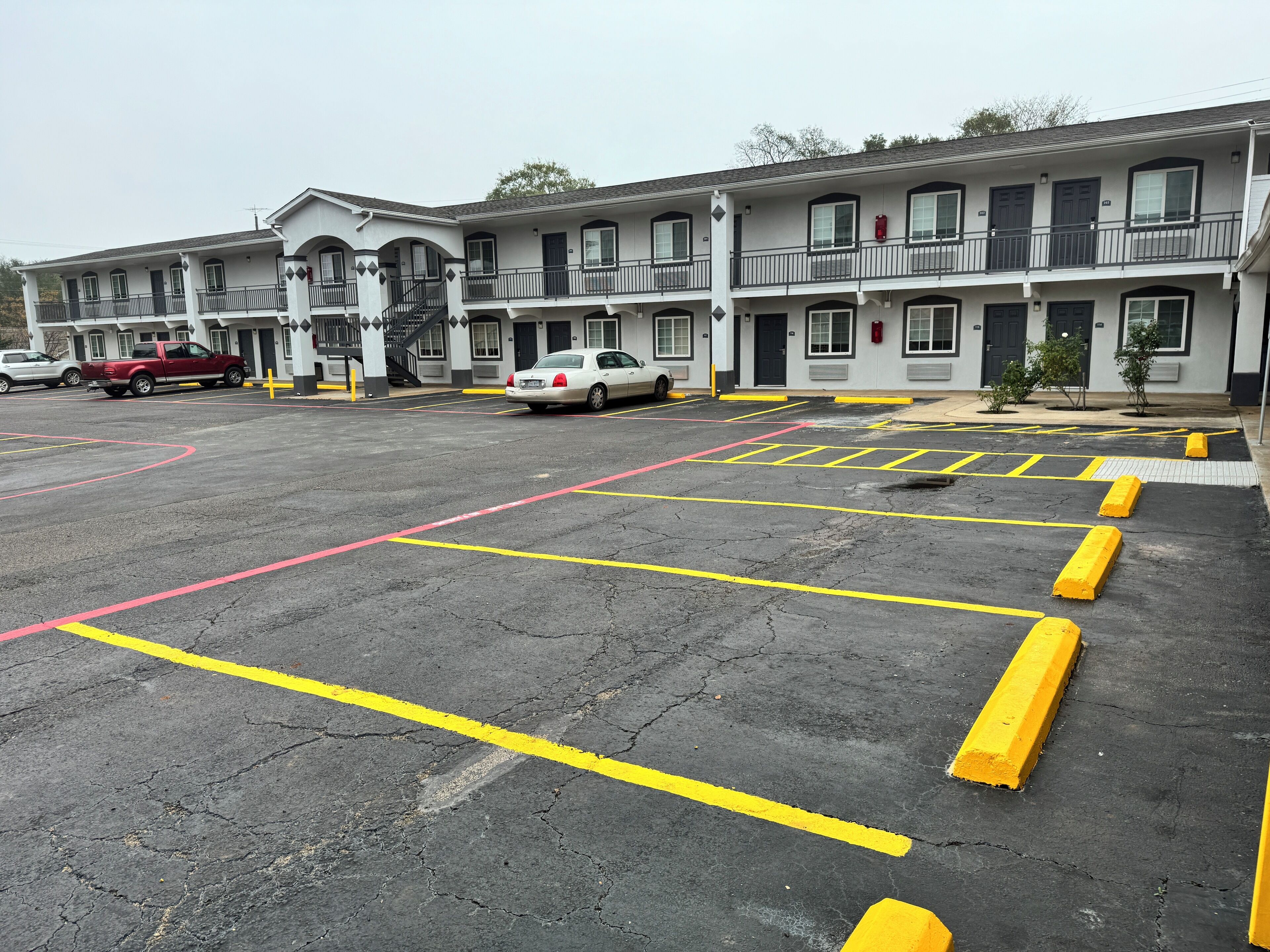 A parking lot with marked spaces and a building with multiple balconies in the background.