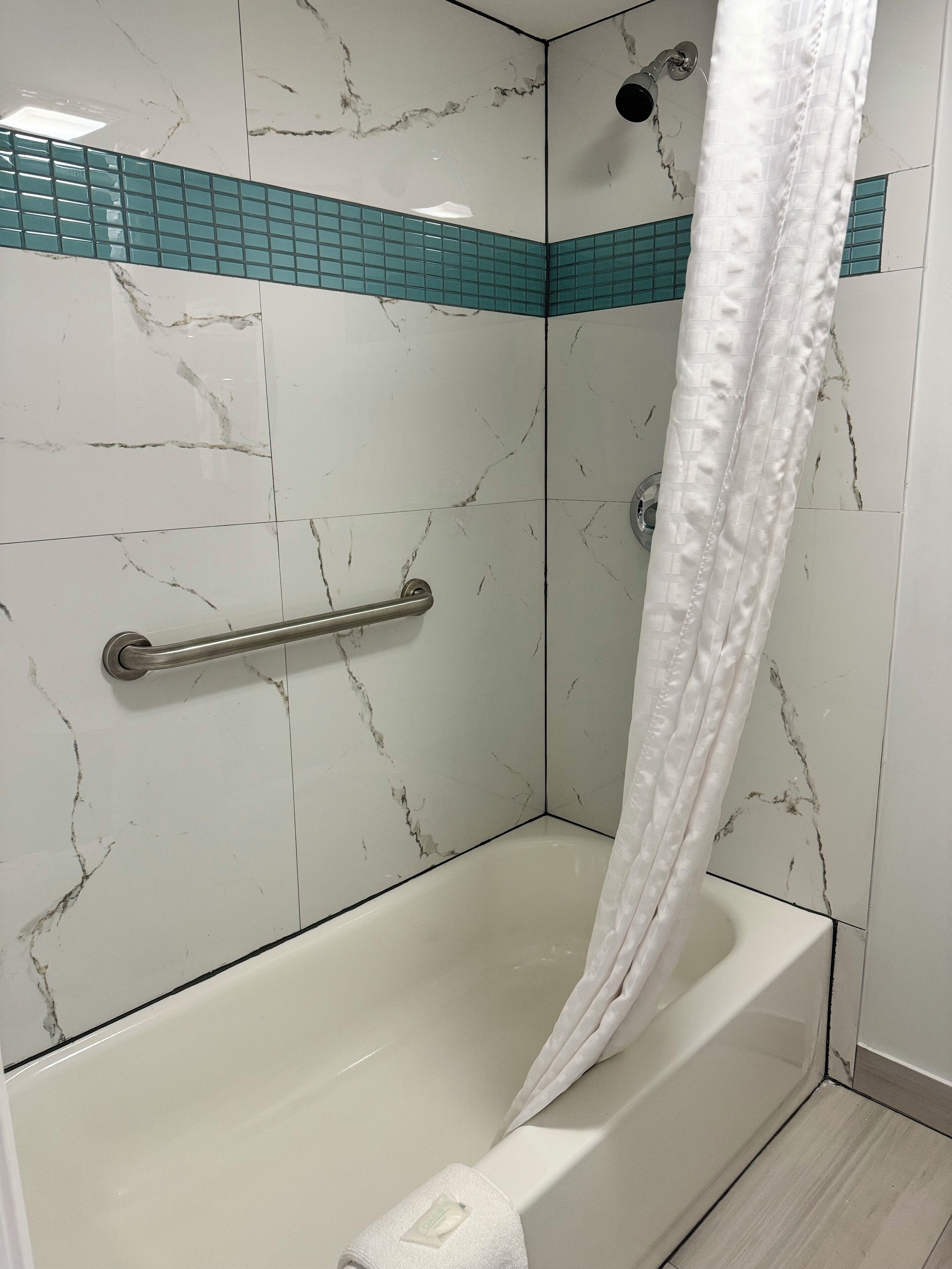 A bathroom with a bathtub, a shower curtain, and a handrail.