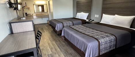 A hotel room with a desk, two beds, a mirror, and a bathroom visible in the background.