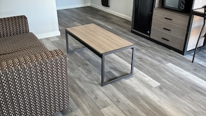 A modern living room with a patterned sofa, a wooden coffee table, and a kitchenette area with a microwave and cabinets. - Continental Inn & Suites Nacogdoches TX / SFA  University/Downtown (Nacogdoches)