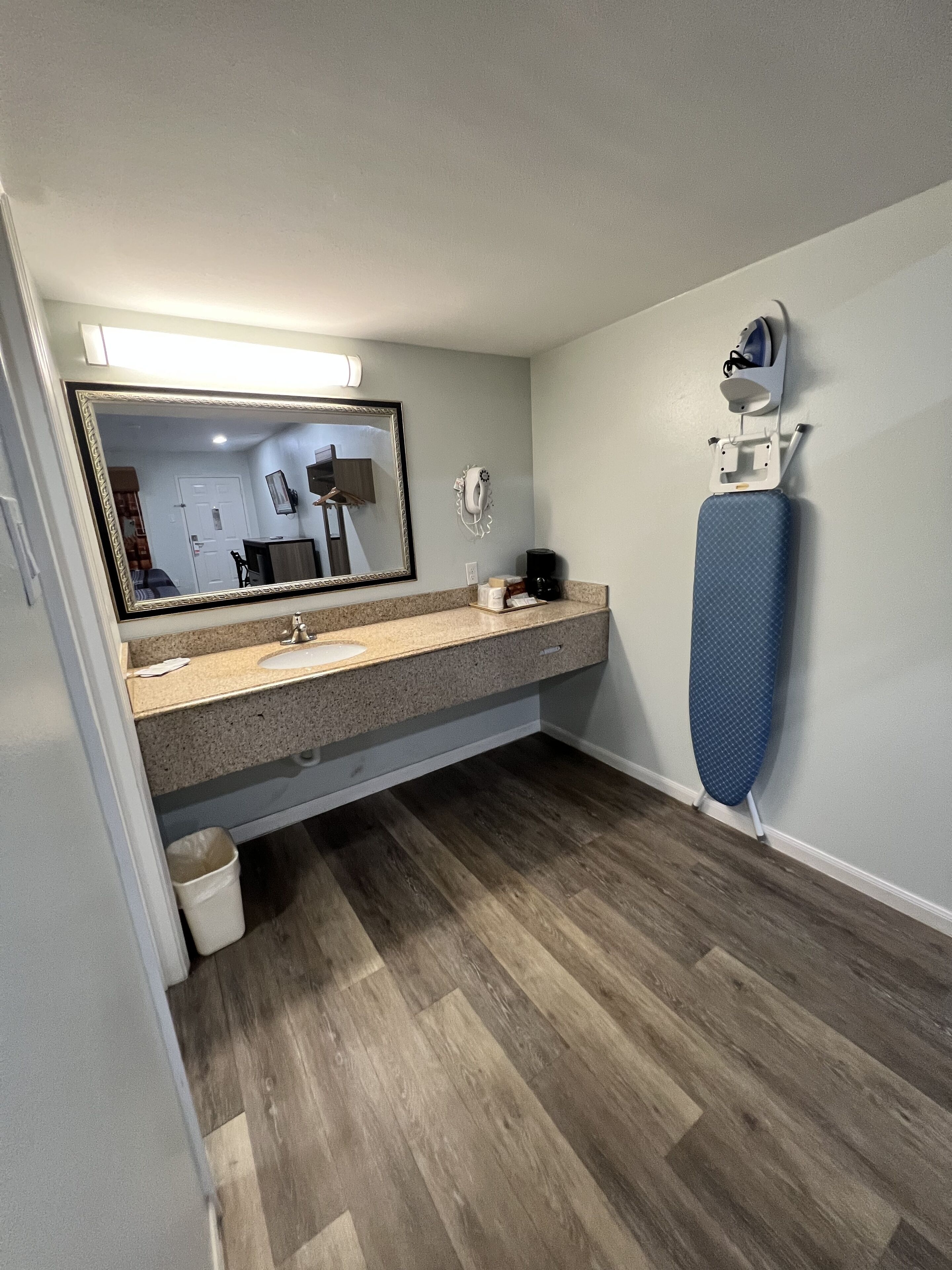 A bathroom with a sink, mirror, and ironing board.