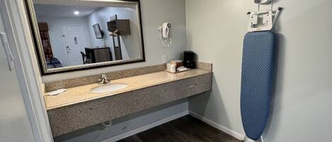 A bathroom with a sink, mirror, and ironing board.