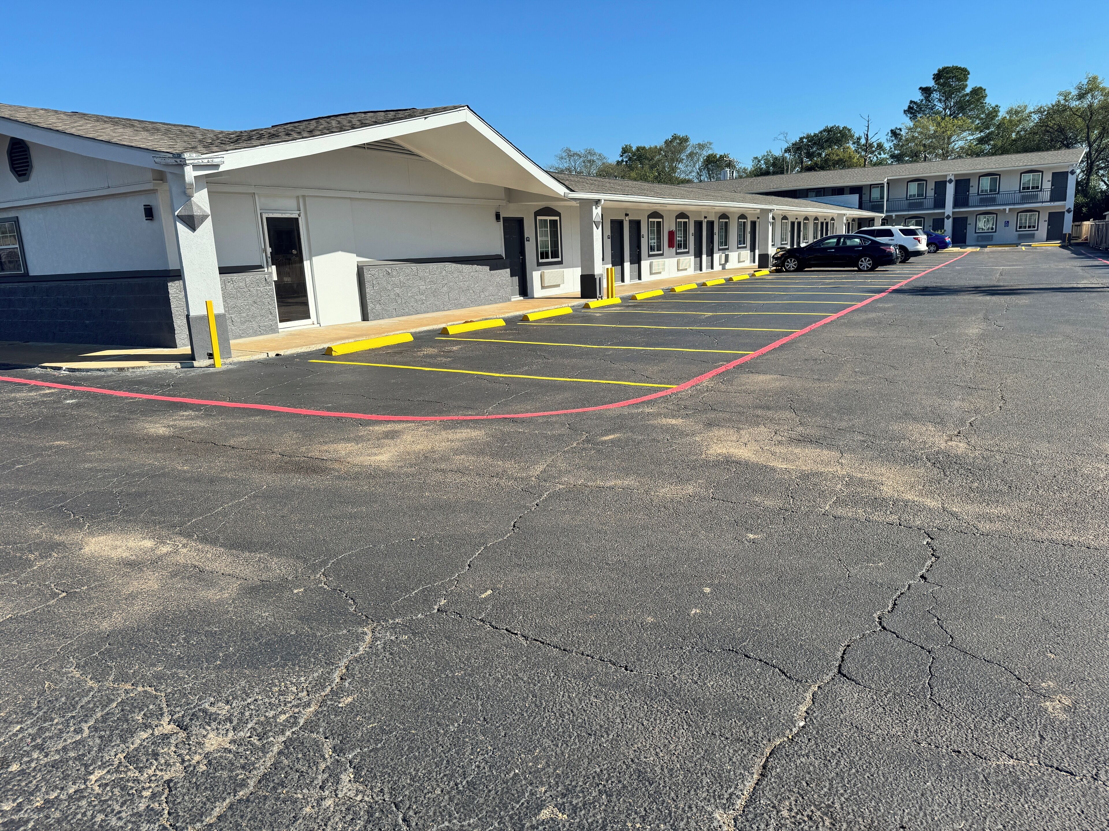 A motel with a row of rooms, a parking lot with marked spaces, and a building with a sloped roof.
