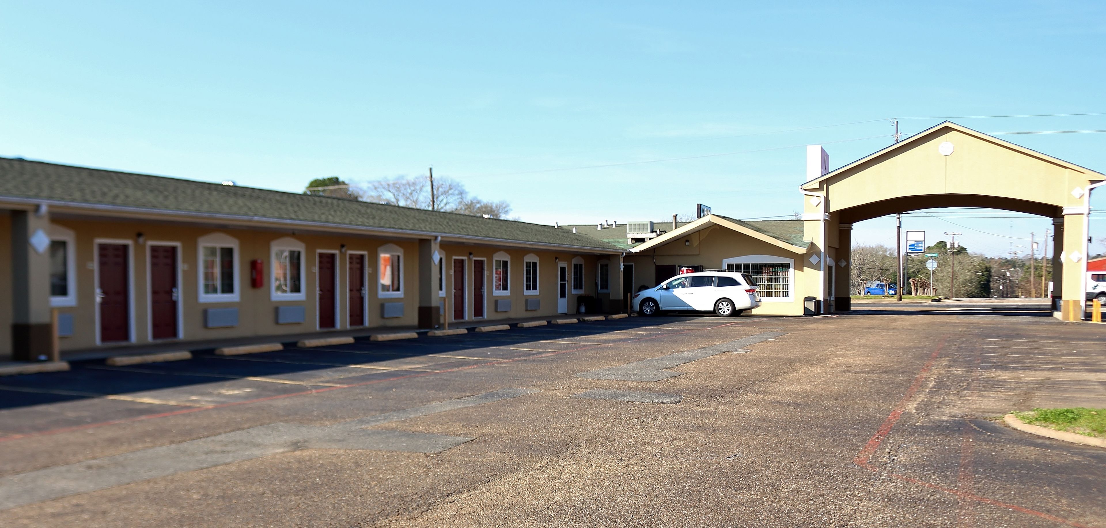 A motel with a row of rooms, a covered parking area, and a white car parked in front.
