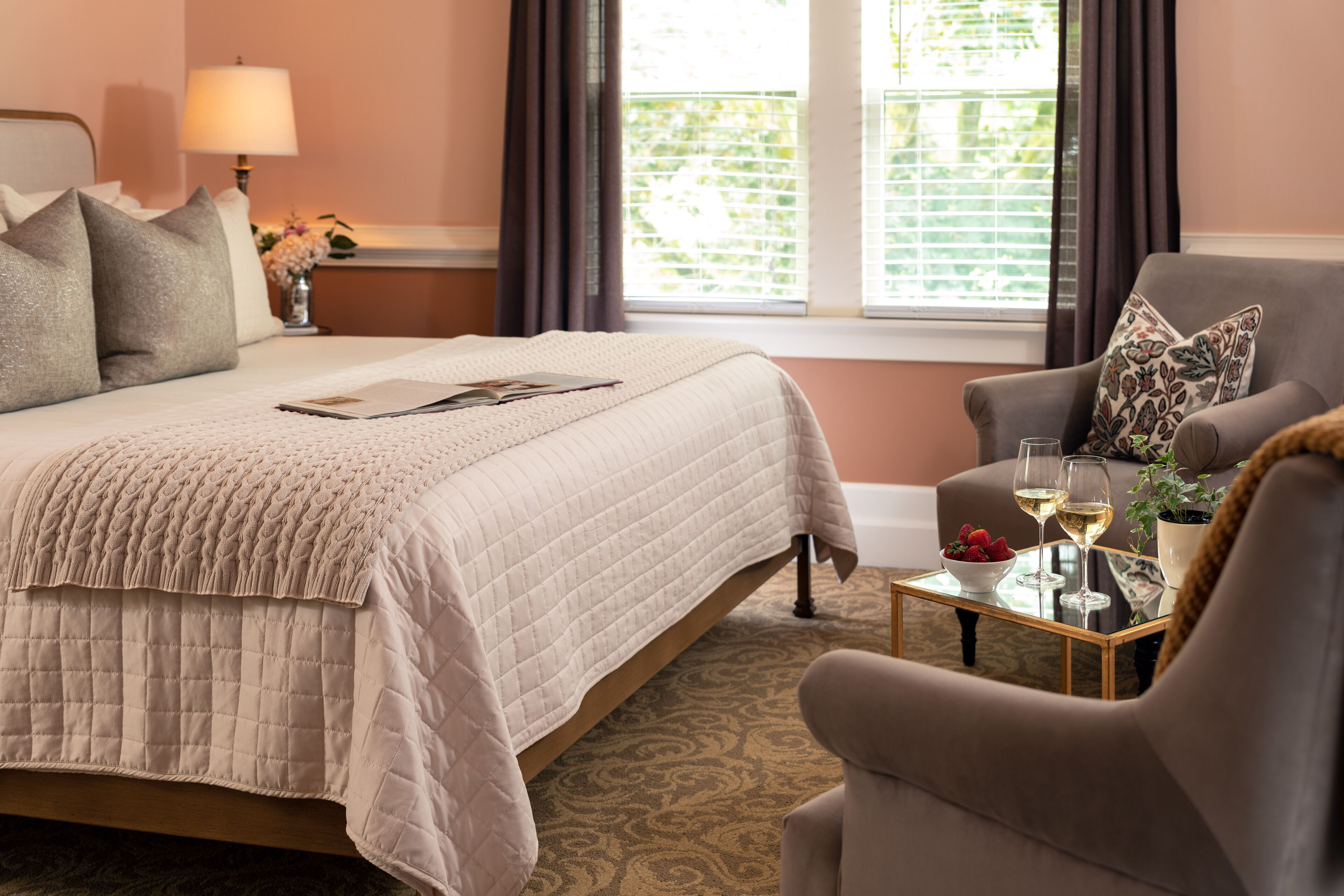 A bedroom with a bed, a chair, a table with glasses, and a window with curtains.