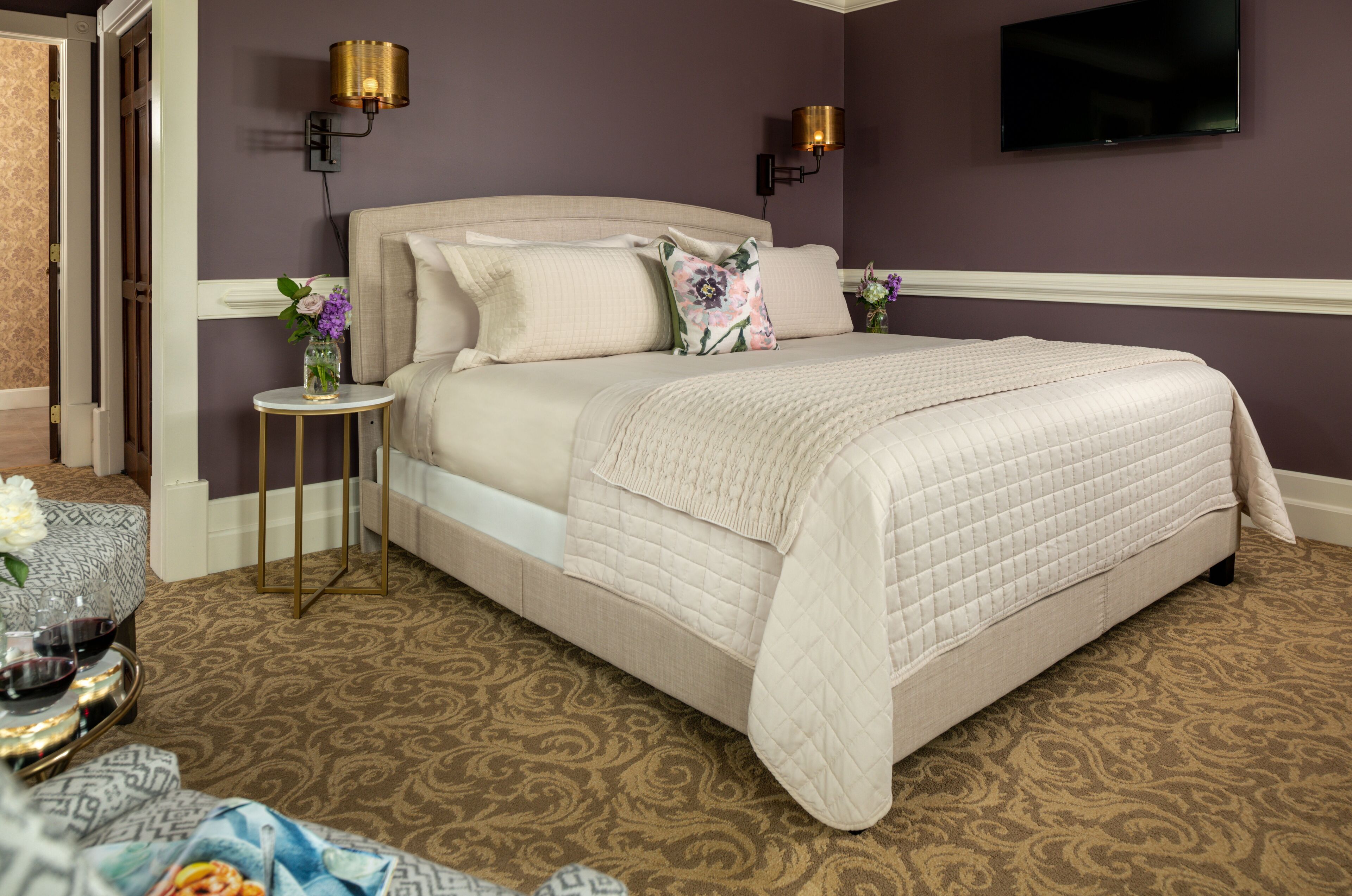 A neatly arranged bedroom with a large bed, two bedside lamps, and a television on the wall.