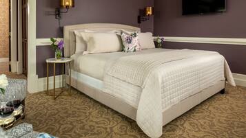A neatly arranged bedroom with a large bed, two bedside lamps, and a television on the wall.