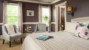 A bedroom with a large bed, two armchairs, a small table with a vase, and a wall-mounted lamp. - The Jacqueline House of Wilmington (New Wilmington)