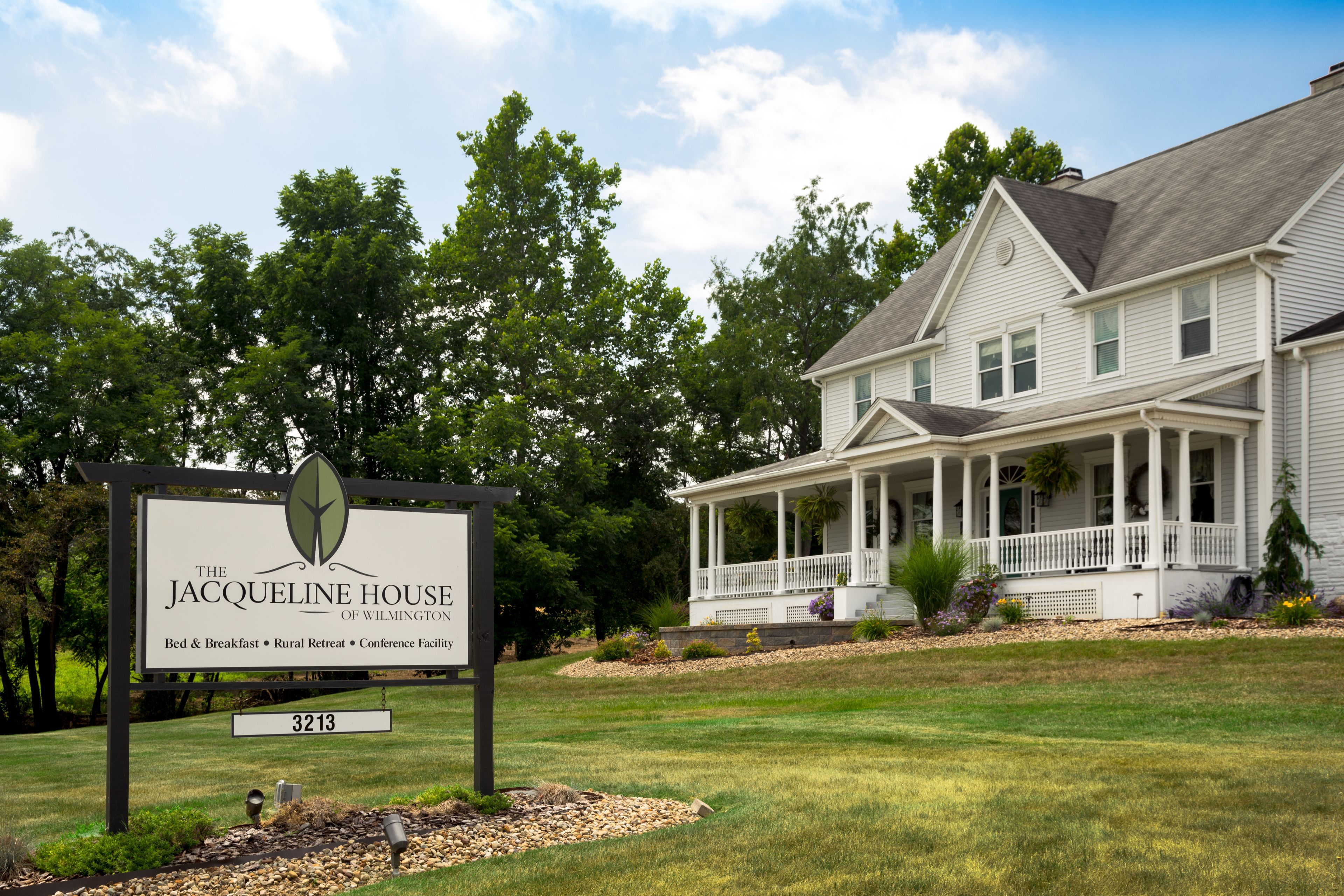 A two-story house with a porch and a sign indicating it is The Jacqueline House of Wilmington, offering bed & breakfast, rural retreat, and conference facility.
