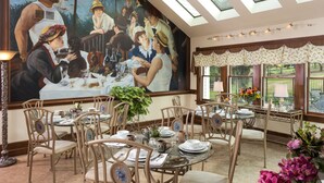 A dining area with a large mural, round tables, and chairs. - The Jacqueline House of Wilmington (New Wilmington)