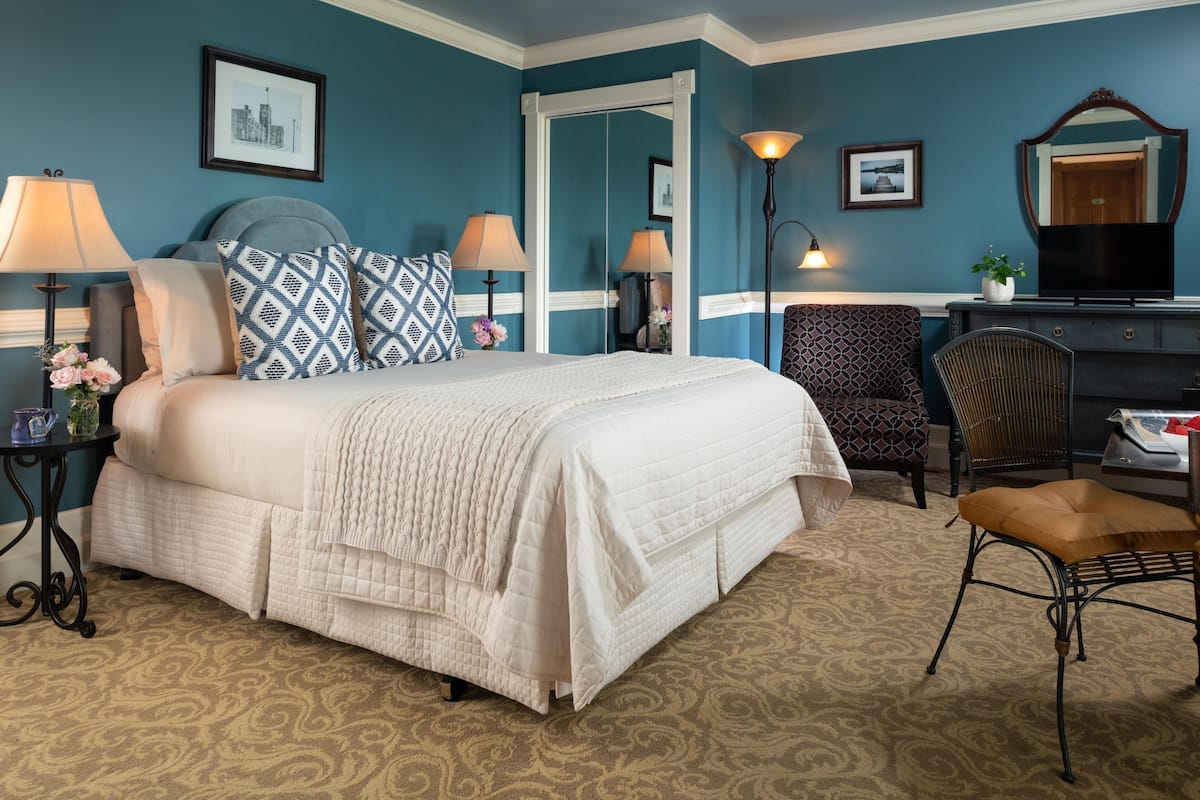 A hotel room with a large bed, two bedside lamps, a chair, a dresser, and a mirror.