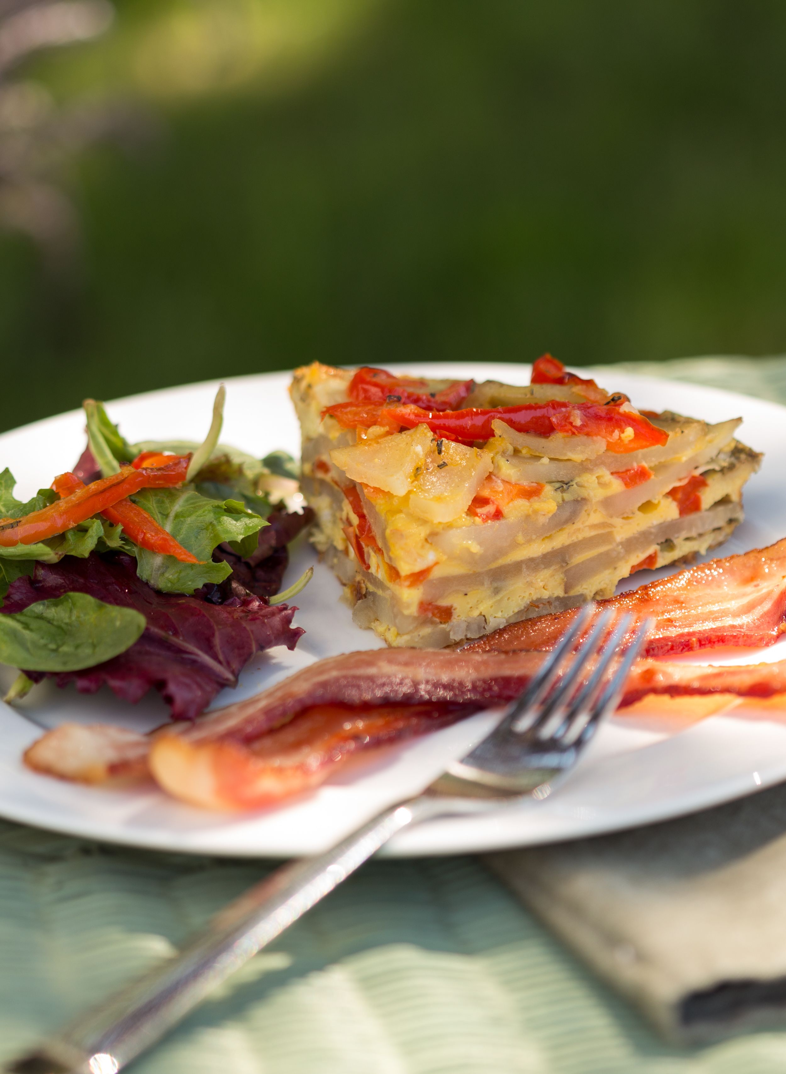Une assiette avec une part de quiche, une salade et une tranche de bacon.