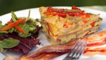 Une assiette avec une part de quiche, une salade et une tranche de bacon.