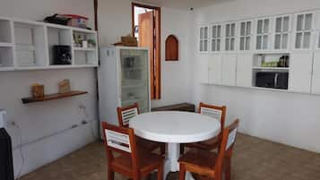 A small dining area with a round table and four wooden chairs, a white refrigerator, and white cabinets with glass doors.