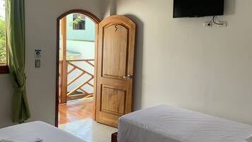 Habitación de hotel con dos camas, un televisor montado en la pared, una puerta de madera y vistas al balcón exterior.