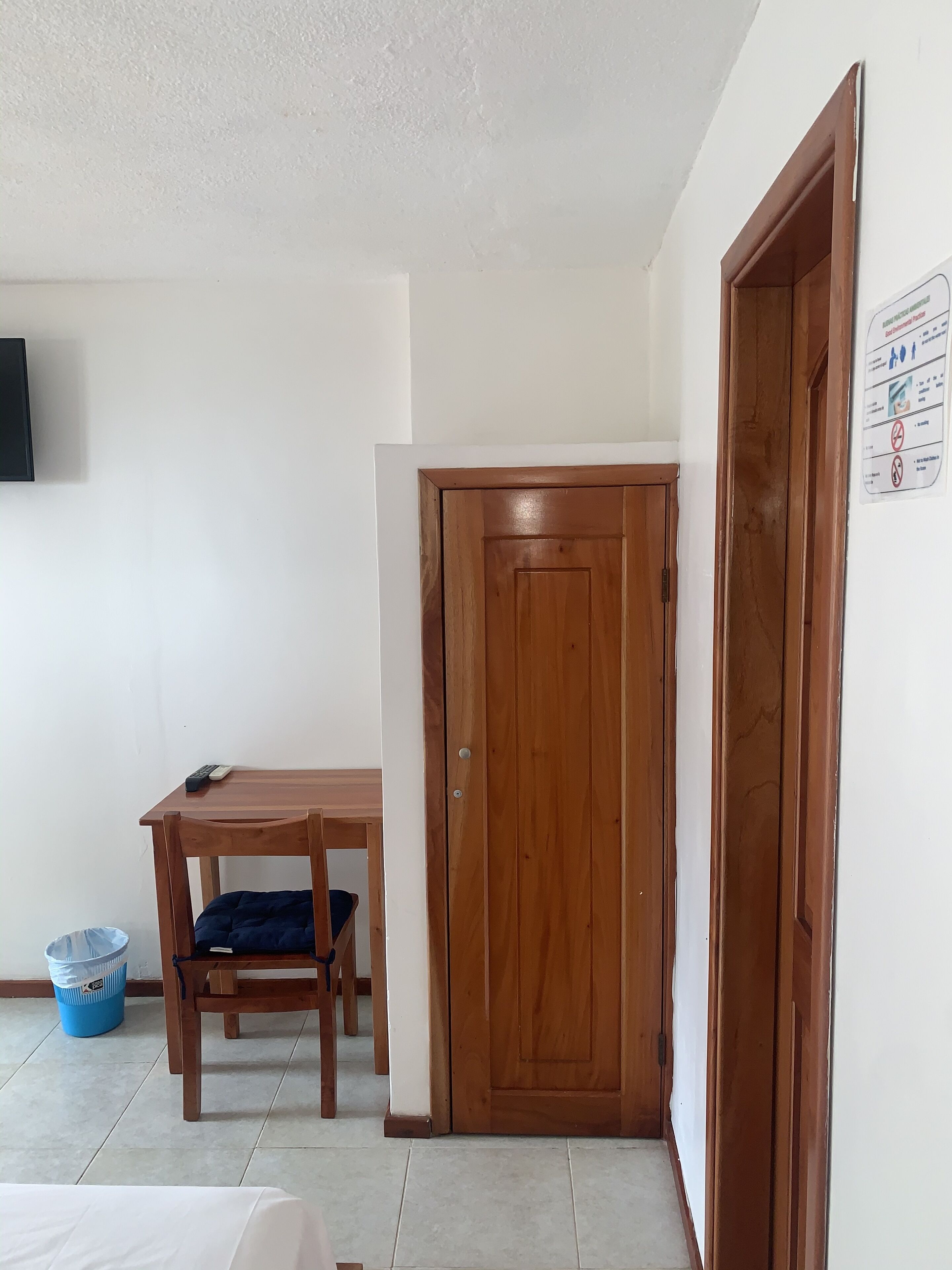 Una habitación con puerta de madera, una mesa con silla y un cubo de basura azul.