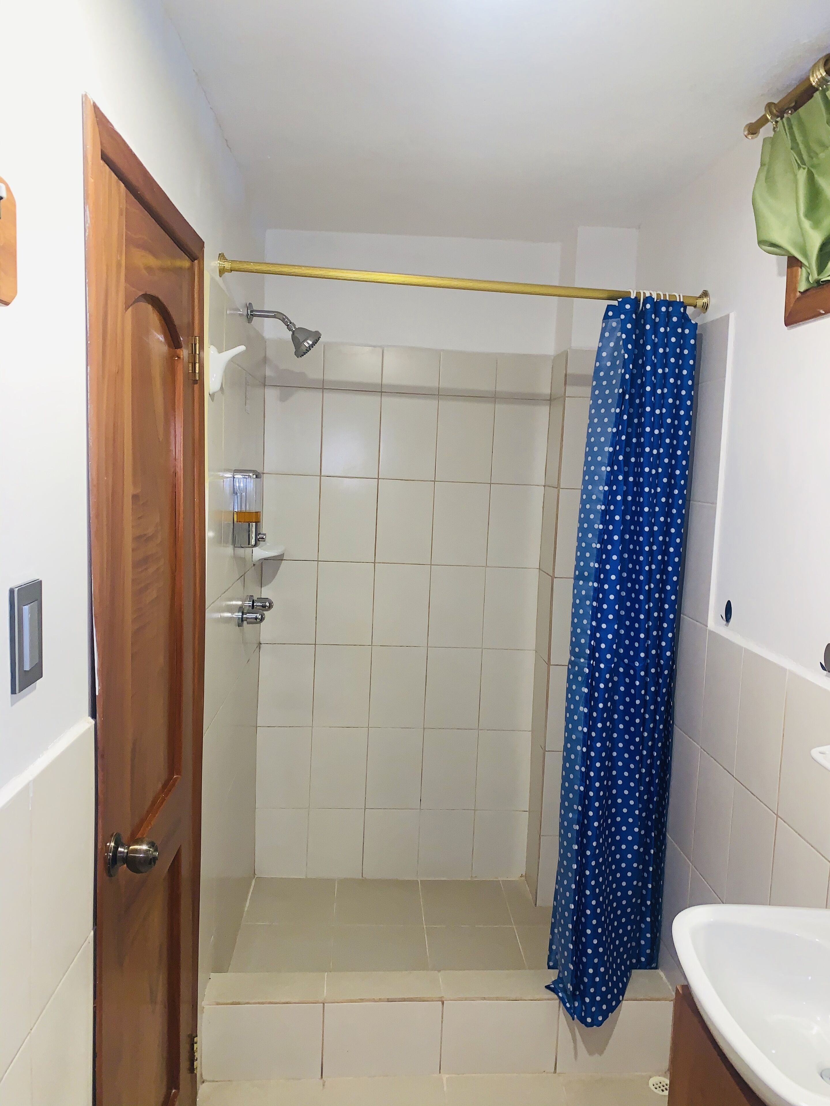 A small, enclosed shower area with a blue polka dot shower curtain, a handheld showerhead, and a wall-mounted light fixture.