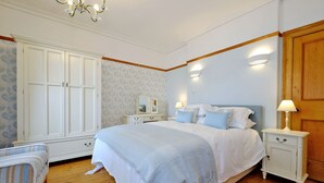 A bedroom with a large bed, a nightstand, a dresser, and a chair. - Aberdeen Lighthouse Cottages (Aberdeen)