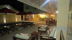 Ein Außenbereich mit Lounge-Möbeln und Sonnenschirmen, ein Schwimmbad und eine Küche im Hintergrund.