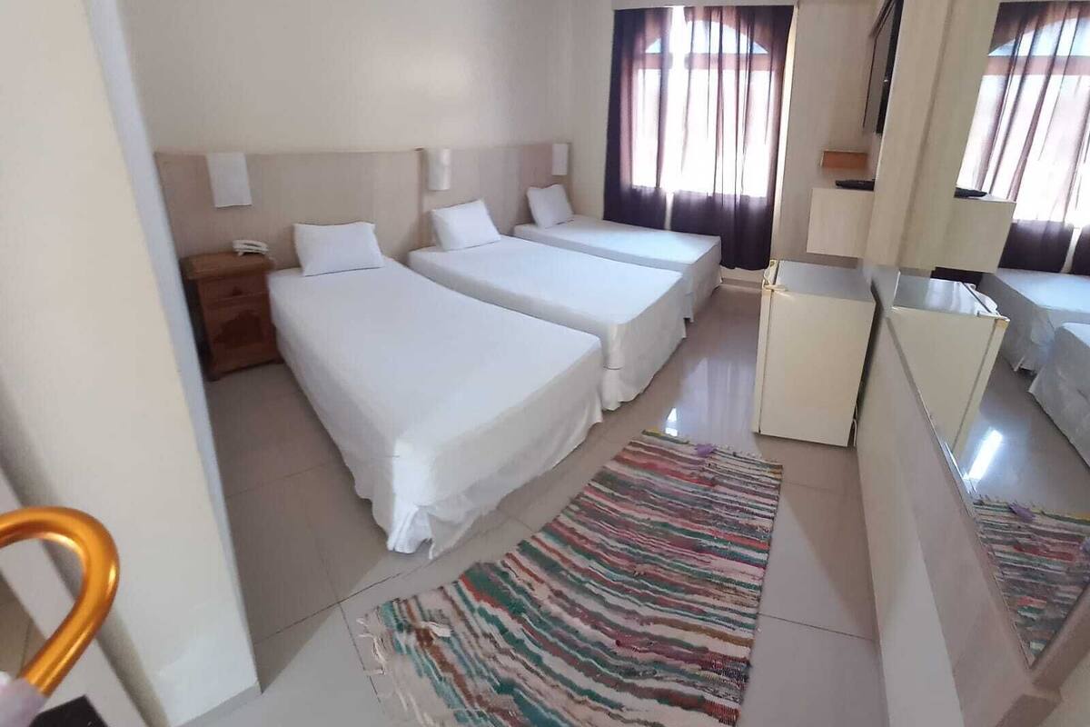 Una habitación de hotel con dos camas, un escritorio pequeño, un espejo y una ventana con cortinas.