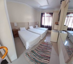 Una habitación de hotel con dos camas, un escritorio pequeño, un espejo y una ventana con cortinas.