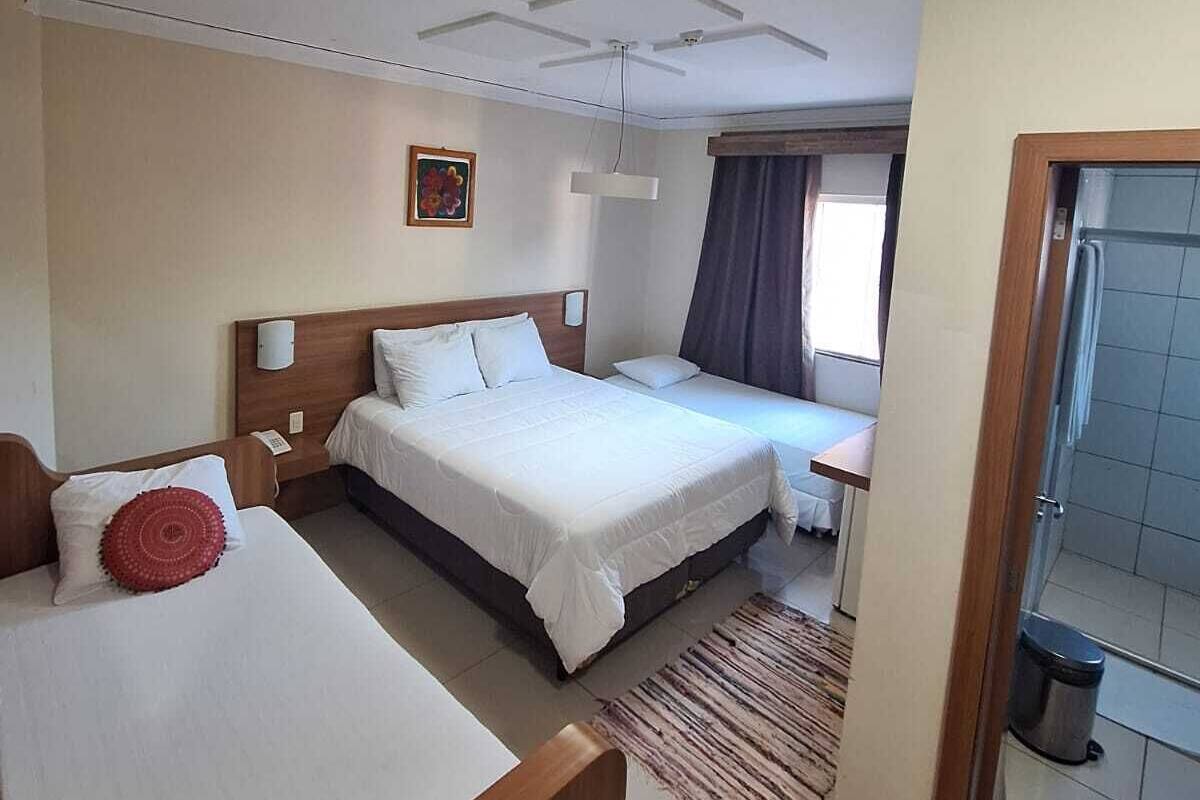 Habitación de hotel con dos camas, un escritorio, una silla, una alfombra pequeña y un baño visible a través de una puerta abierta.