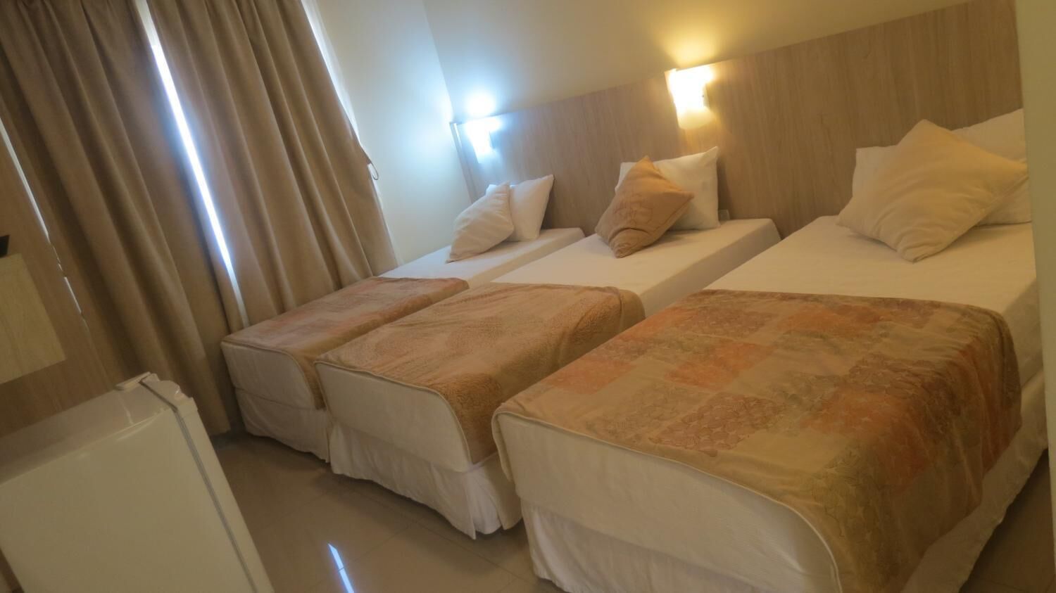 A hotel room with two single beds, a wooden headboard, and a small white appliance.