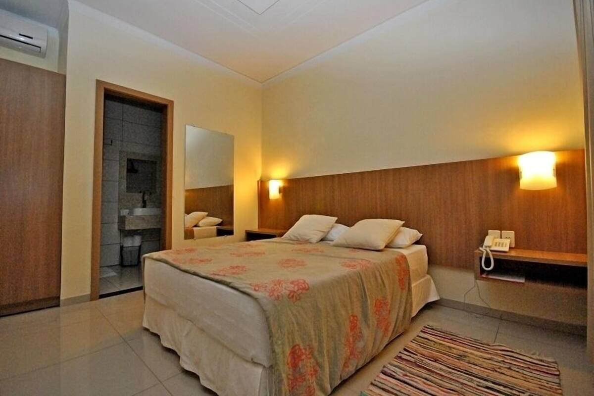 Un dormitorio con cama, mesitas de noche, un espejo y un teléfono.