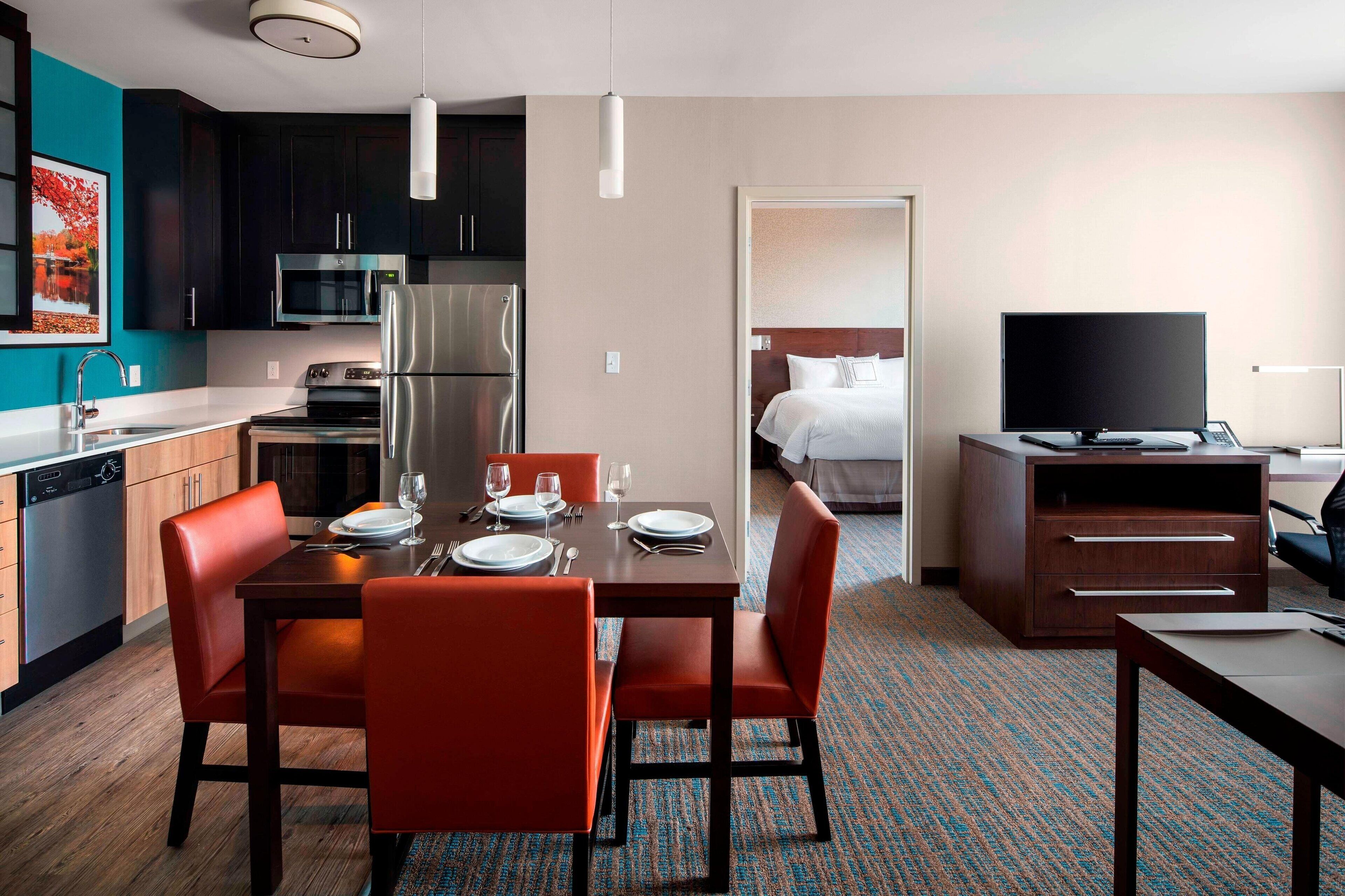 A modern hotel room with a kitchen, dining area, and a bed.