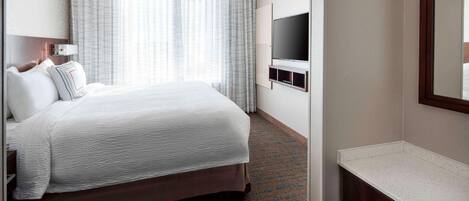 A hotel room with a large bed, a TV mounted on the wall, and a bathroom with a countertop.