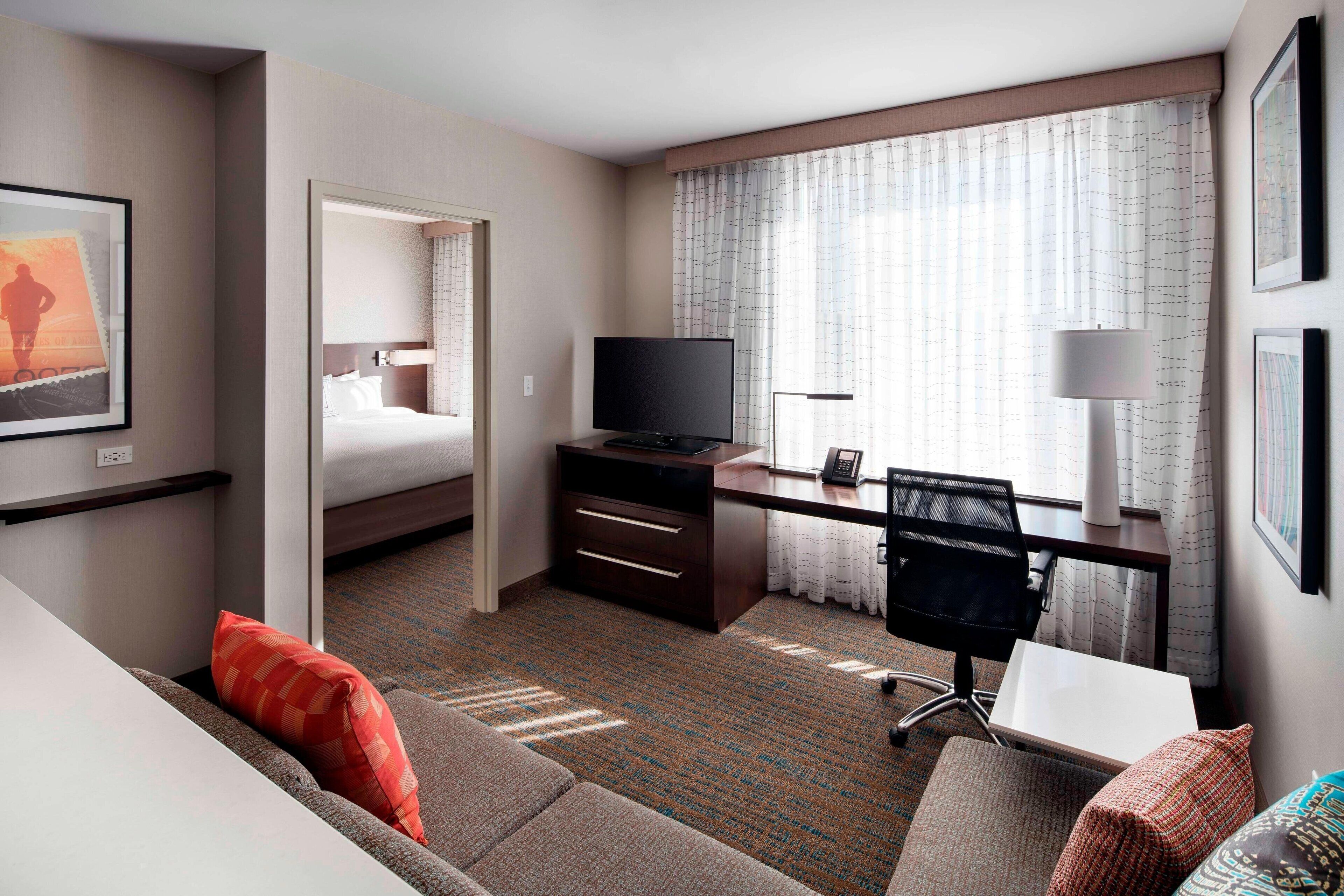 Une chambre d’hôtel avec un lit, un bureau avec une télévision, une chaise, un canapé et une fenêtre avec des rideaux.