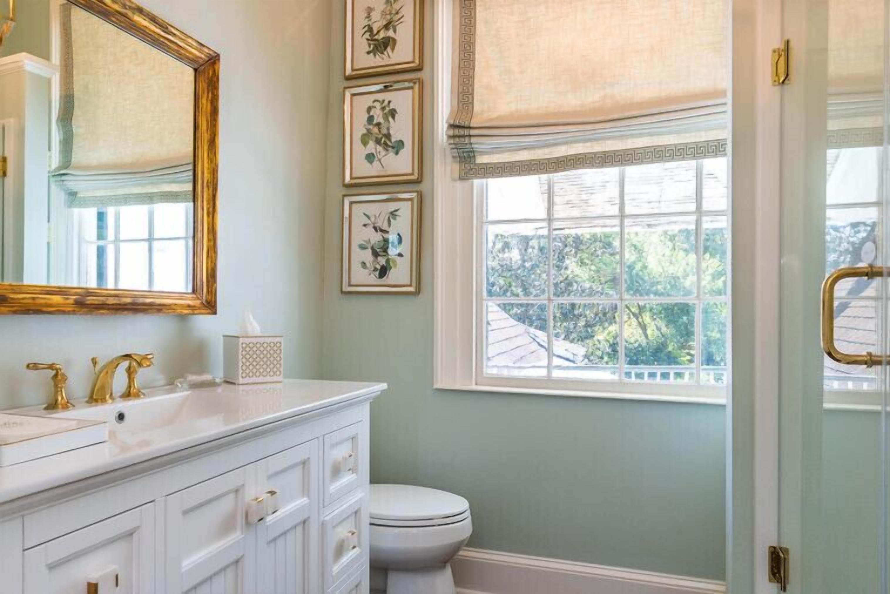 A bathroom with a white vanity, a large mirror, and a window with a view of trees.